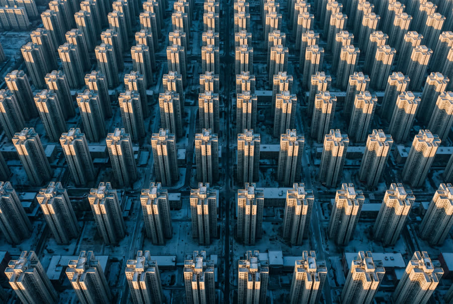 Dense rows of identical residential towers from directly above at first light, long parallel shadows