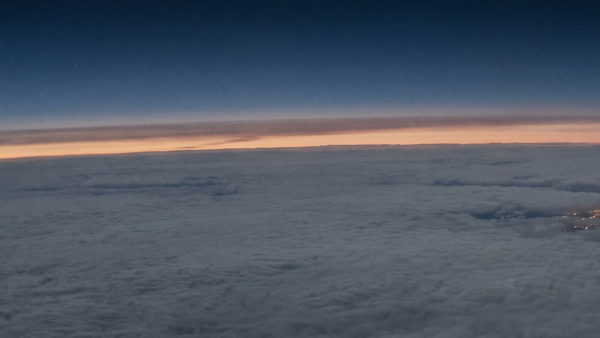 A sea of cloud at first light, with a thin band of dawn along the horizon, seen from high altitude.
