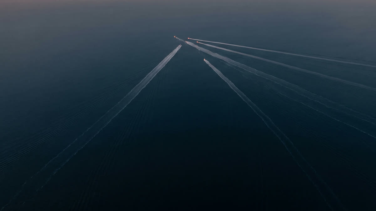 The wakes of several ships converging on dark water, seen from above.