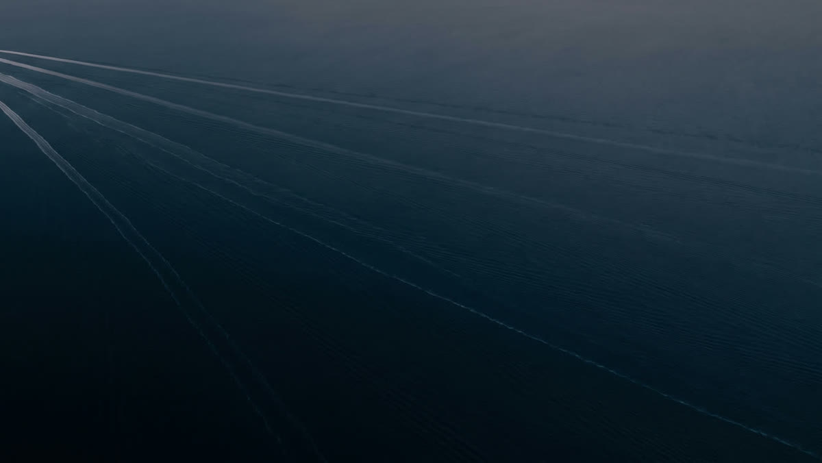 Long, straight ship wakes crossing dark water, seen from above.